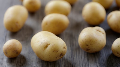 Close-up of several small, unpeeled potatoes scattered across a dark wooden surface