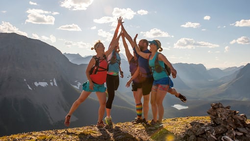 A group of trail runners are all high-fiving each other at the top of a mountain overlook. 