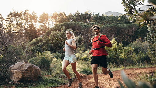 A man and a woman are trail running in a very lush canyon.