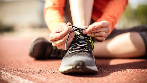 person tying their running shoe on a outdoor track
