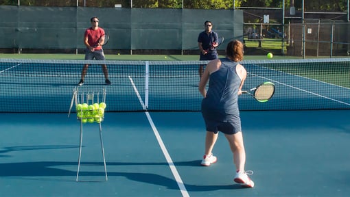 three people playing tennis outside on a tennis court