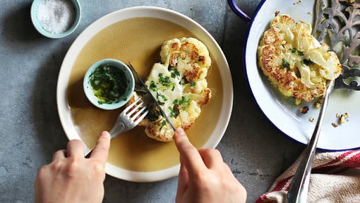 cauliflower steak with someone using a fork and knife to cut it