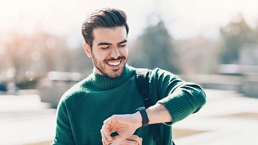 man in a green sweater outside looking happily at his watch