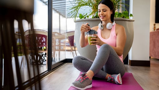 woman in a pink shirt sitting on a yoga mat on the ground enjoying a post workout snack