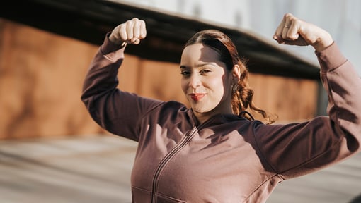 Woman standing outside smiling and flexing her arms over her head