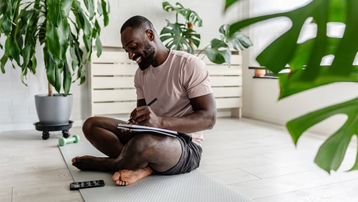 man sitting on the ground on a yoga mat doing some healthy intentional journaling