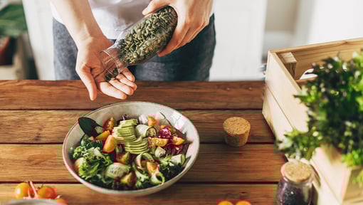 person pouring out seeds from a jar to add to a plant based salad