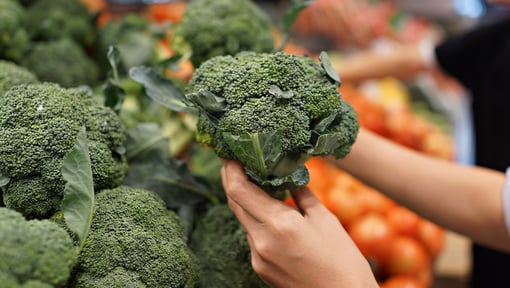broccoli in someones hand in the produce isle of a grocery store
