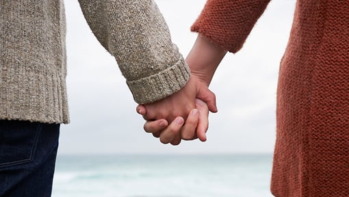 back of two people holding hands in front of the ocean