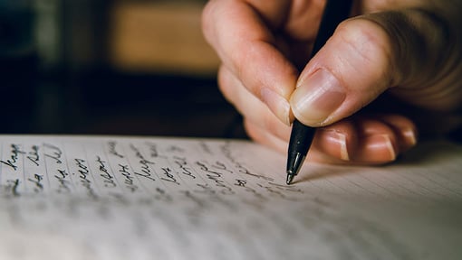 Hand writing in a journal with a pen, close-up view.