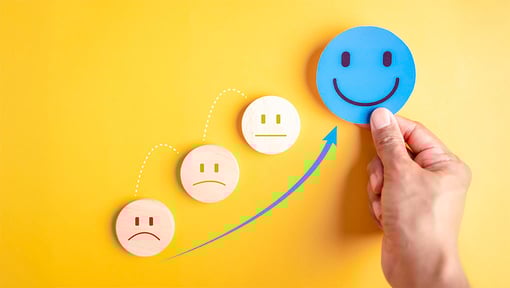 A hand holds a happy blue face above a sequence of emotional faces, showing a progression from sad to happy.