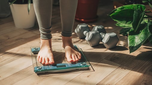 Woman with dumbbells standing on scale 