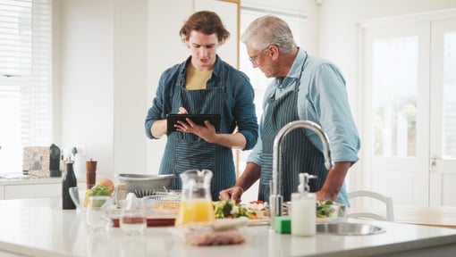 Two men in a modern kitchen preparing food using fresh ingredients.