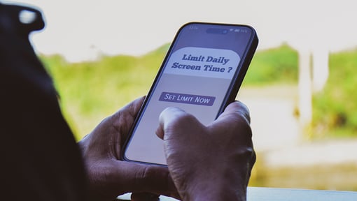 ose-up of hands holding a smartphone displaying a screen with the message “Limit Daily Screen Time?” and a button labeled “Set Limit Now.” 