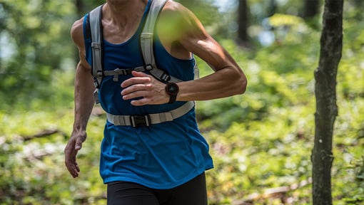 Person running outdoors on a forest trail while wearing a weighted backpack.
