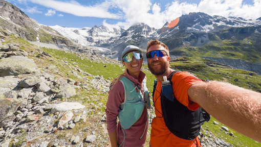 Two people posing for a picture standing on a rocky mountain trail.