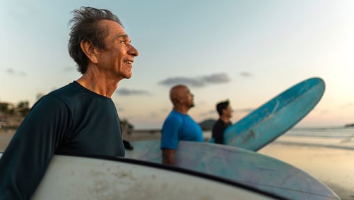 Three people standing on a beach with surfboards, preparing to head into the ocean.