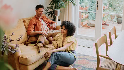 Two people relaxing at home with their dog. The casual scene reflects taking time to recover in the days after a trip, stressing the importance of building rest days into travel timelines. 
