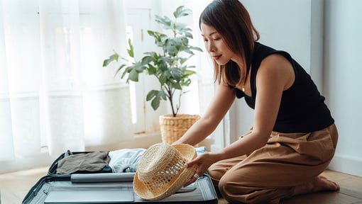 A millennial woman kneeling on the floor while packing for a trip, she is trying to pack light. 