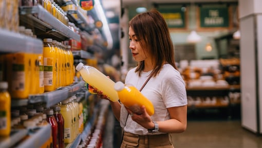 A woman examining the labels on two different juices in the grocery store. 