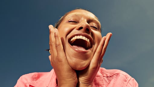 Person resting hands against the face, while smiling with an open mouth.