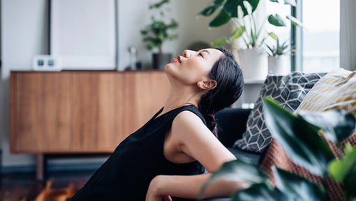 A woman leaning back on her couch while doing a self-compassion mantra in her head. 