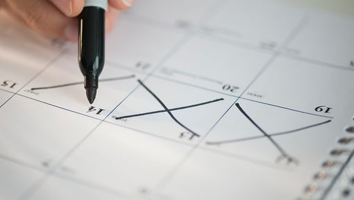 Close-up of a hand holding a marker crossing out days on a monthly calendar page.