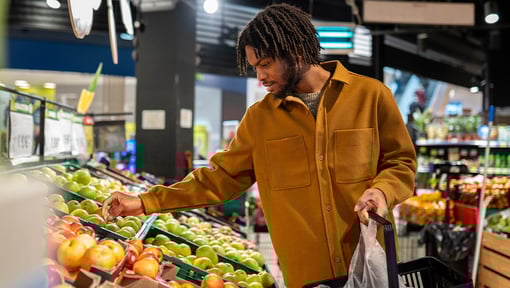 Shopper selecting fresh produce while shopping for whole foods in a grocery store produce section.