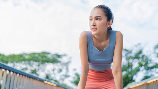 A woman taking a breath and resting her hands on her knees after finishing a LISS workout