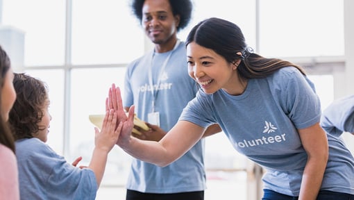 Volunteers interact with children in a bright indoor space, sharing a high‑five during a community volunteering activity.