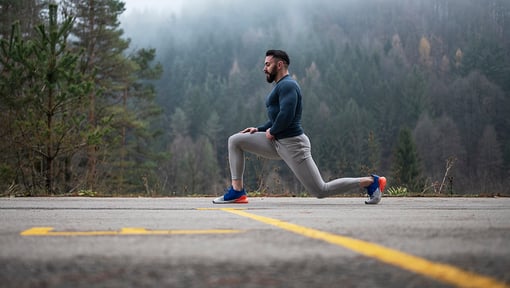 A man doing a forward lunge stretch outdoors on a road