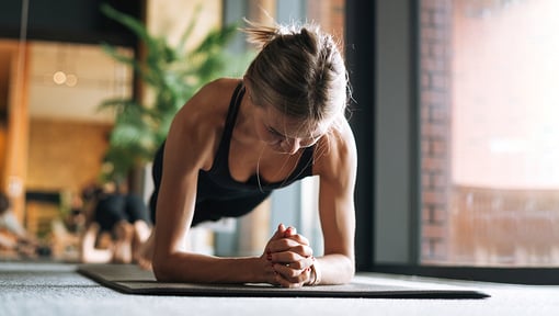 A woman holding a forearm plank on a yoga mat indoors during a quick workout.