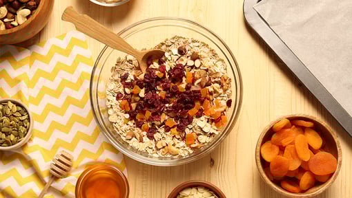 Overhead view of bowls filled with no bake granola bar ingredients including oats, dried fruit, and nuts, seeds, dried apricots, and honey.