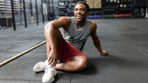 A man smiling while sitting on the floor at a gym after a workout