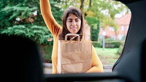 Woman placing a paper grocery bag into the open trunk of a car.
