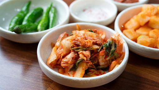 Small bowls of fermented foods on a table, including kimchi, pickled vegetables, and green peppers.