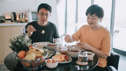 Two people seated at a table enjoying a balanced meal with fruits, bowls of food, and water
