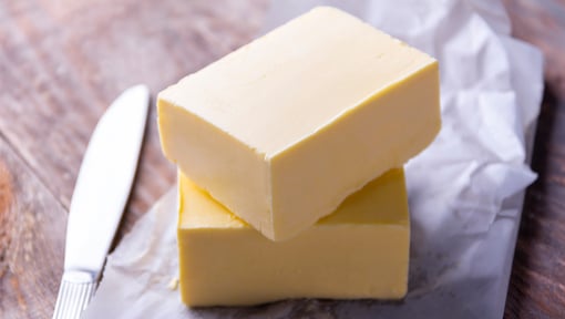 A block of butter set on parchment paper on a wood surface, a butter knife is sat next to the butter. 
