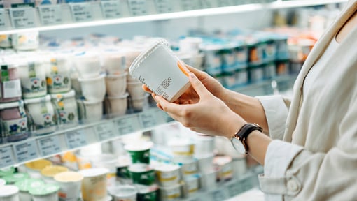 A person holding a yogurt container in the dairy isle of a grocery store. 