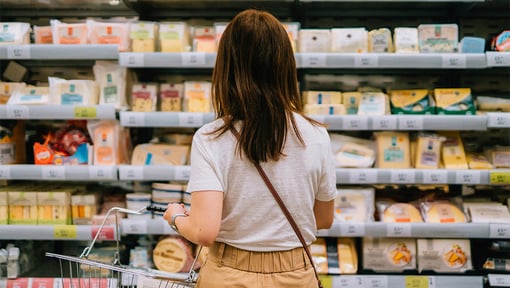 The back of a person looking at different cheeses in the dairy isle of a grocery store