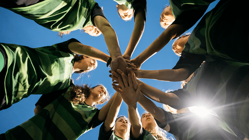 A sports team in a circle with their hands all in about to do a team chant. 