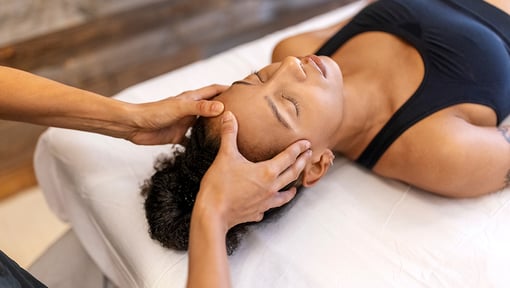 A woman receiving a neck and head massage while lying on a treatment table.