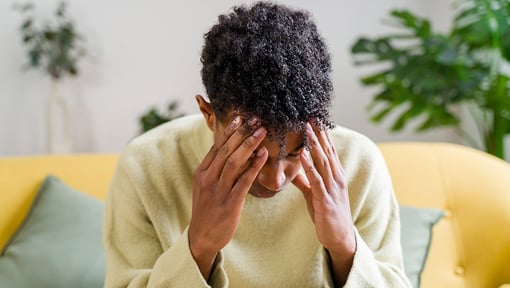 Person sitting on a couch holding both temples, a common visual representation of headache.