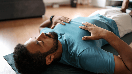 A man lays on a yoga mat while doing one minute of mindful breathing