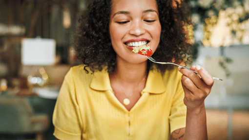 A woman holds a fork up to her mouth, the fork has salad on it.