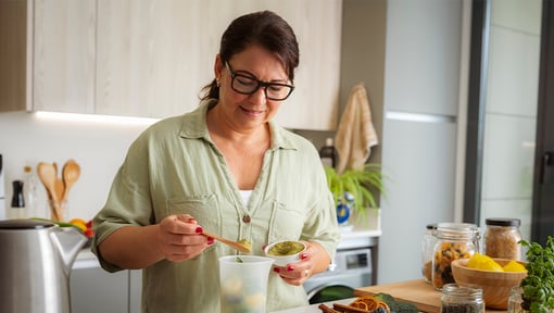 A woman in her kitchen measuring some ground superfood powder into a container.