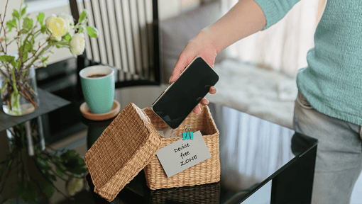 a person putting their smart phone in a box that states device free zone.