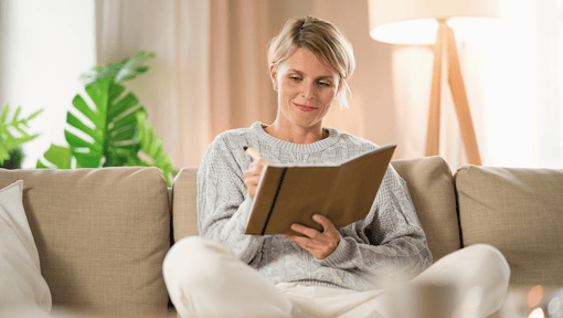 A woman sitting on her couch writing in a journal. 