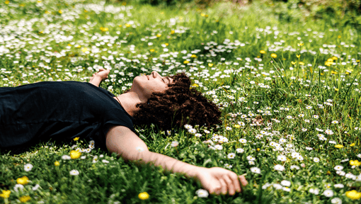 A person laying with their arms open in a meadow of wild flowers. 