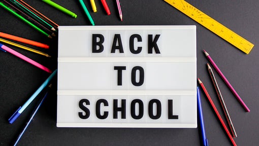 Back to school sign on a black background with colored pencils, a ruler, and pens.